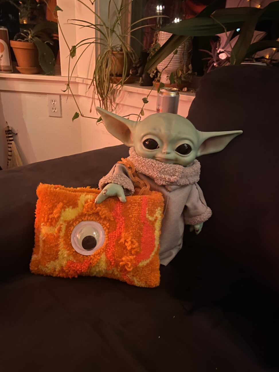 Baby Yoda doll holding an orange purse with an eyeball on it.
